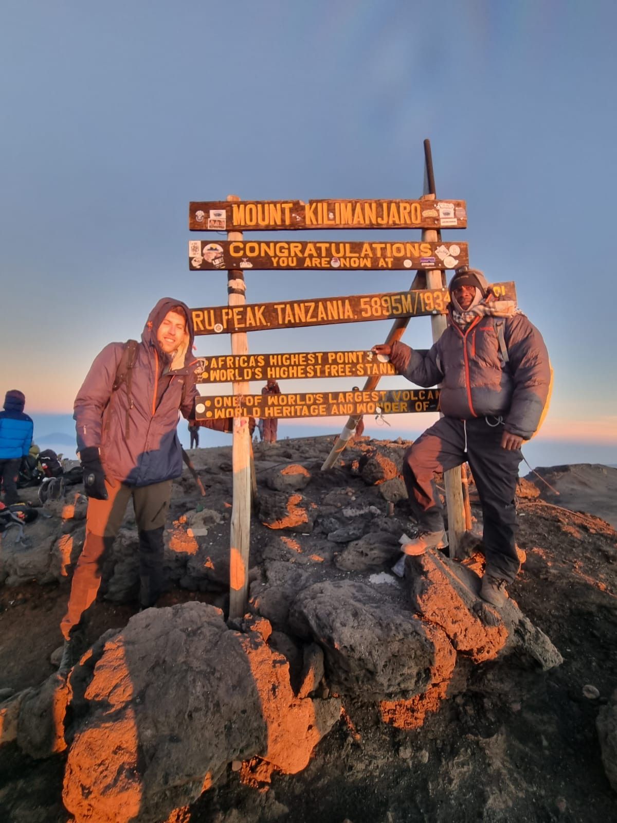 A climber and guide at the Uhuru Peak sign at sunrise